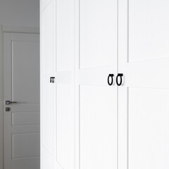 White wooden wardrobe with black handles. The interior of the apartment is in Scandinavian style