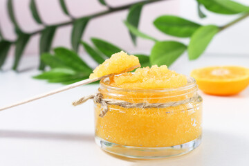 Body scrub with citruses front view. Cosmetic product for spa procedures and skin cleansing on a wooden table with green leaves of the plant.