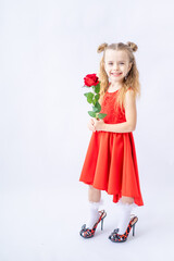 a little happy child girl in a red dress and in her mother's big shoes with a rose in her hand on a white isolated background laughs and smiles, the concept of Valentine's day, a place for text