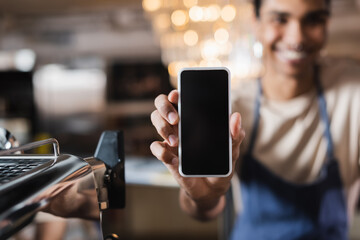 Smartphone with blank screen in hand of blurred african american barista in cafe.