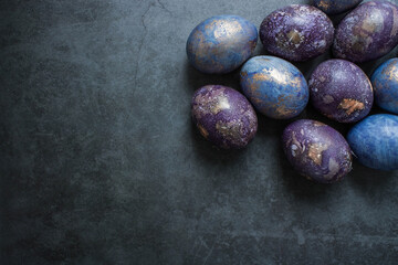 Easter card with a copy of the place for the text. Purple, blue and golden eggs on a dark background. The trend of 2022 purple shade is very peri. Natural dye karkade tea. Top view.