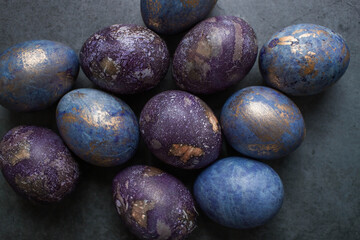 Easter card with a copy of the place for the text. Purple, blue and golden eggs on a dark background. The trend of 2022 purple shade is very peri. Natural dye karkade tea. Top view.