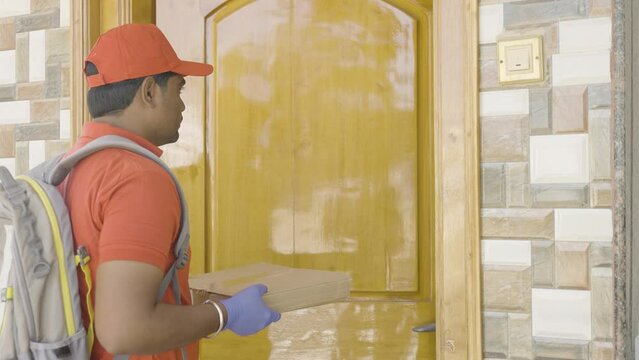 Young indian delivery boy giving parcel to consumer after opening door- concept of fast Home delivery and online e-commerce shopping