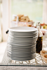 lots of white plates in a stack on the dining room table.