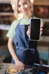 Smartphone with blank screen in hand of blurred barista in cafe.