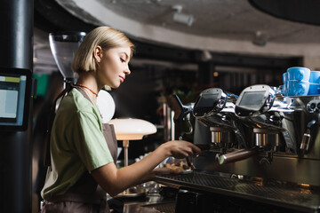 Fototapeta na wymiar Side view of young barista working with coffee machine in cafe.