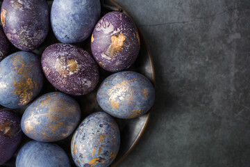 Easter card with a copy of the place for the text. Purple, blue and golden eggs in an iron plate on a dark background. The purple hue trend of 2022 is veryperi. Natural dye karkade tea. Top view.