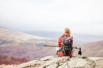 Hiker girl taking a rest on a rock in the mountains. Windy day. Travel and healthy lifestyle outdoors in fall season