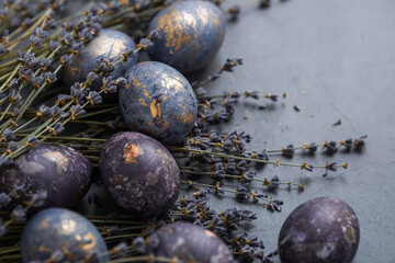 Easter card with a copy of the place for the text. Purple, blue and golden eggs with lavender on a dark background. The purple hue trend of 2022 is very relevant. Natural dye karkade tea. Top view.