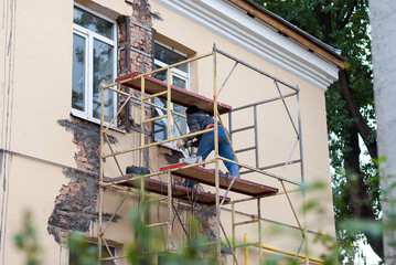 A man repairs the wall of a house on the street.