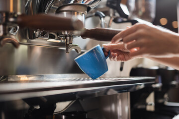 Cropped view of barista holding cup near portafilter of coffee machine in cafe.