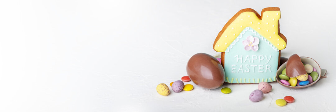 Broken Easter Chocolate Eggs, House Shaped Cookie And Colorful Decorations On A Light Background. Banner. Easter Concept, Easter Treats. Flat Lay, Top View.