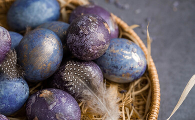 Easter card with a copy of the place for the text. Purple, blue and golden eggs in a basket on a dark background. The purple hue trend of 2022 is very peri. Natural dye karkade tea. Top view.