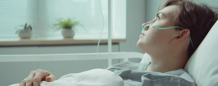 Young female patient with nasal cannula lying on bed in hospital ward during therapy