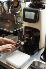 Cropped view of barista holding portafilter near grinder in cafe.