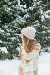 Fototapeta na wymiar Beautiful young woman holding a retro vintage film camera for taking photos in winter snowy forest. Hobby and leisure activity outside. Hipster stylish girl in beanie hat in winter outdoors near fir.