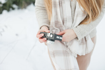 Unrecognizable woman holding a retro vintage film camera for taking photos in winter snowy forest. Hobby and leisure activity outside. Hipster stylish girl in winter outdoors close up.