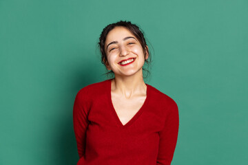 Fototapeta premium Happy young pretty girl in red pullover isolated on green background. Concept of emotions, facial expressions