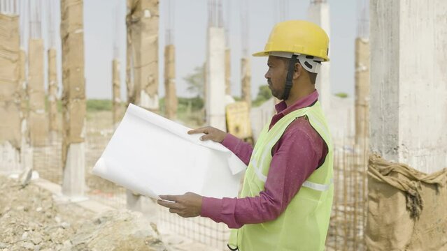 young indian engineer or supervioser inspecting construction plan at workplace - concept of skilled labour,daily wager lifestyle and construcation service.