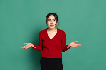 Annoyed young pretty girl in red pullover isolated on green background. Concept of emotions, facial expressions