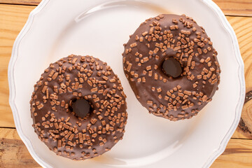 Two sweet chocolate donuts on a white saucer, macro, top view.