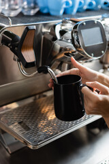 Cropped view of barista holding jug near steam wand of coffee machine in restaurant.