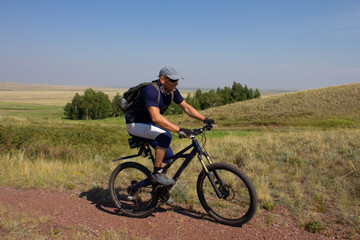 Smiling man with the backpack travelling by bicycle along the steppe road. Active leisure concept.