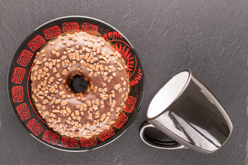 One sweet chocolate donut on a black saucer with a cup, on a slate rock , macro, top view.