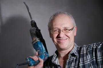 Portrait of a man 55-60 years old in a working environment during the repair of an apartment with his own hands, in a plaid shirt, smiling, wearing glasses, holding a perforator