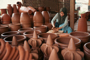 Fototapeta na wymiar young woman in headscarf sitting working clay among pottery