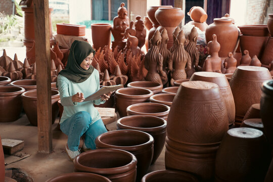Veiled woman holding clipboard while counting pottery ceramics