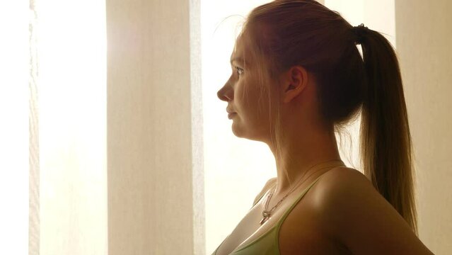 Pregnant blonde woman looking out At window and caressing her stomach. She is calm and very relaxed