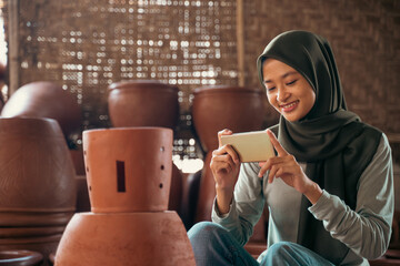 girl in hijab using mobile phone to photograph clay products
