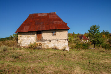 Traditional stone house in mountain during winter. Old stone and wooden house in nature. Rusty tin roof on abandoned house in village.