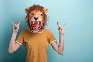 Woman in lion mask with hands in rock sign, isolated on blue background