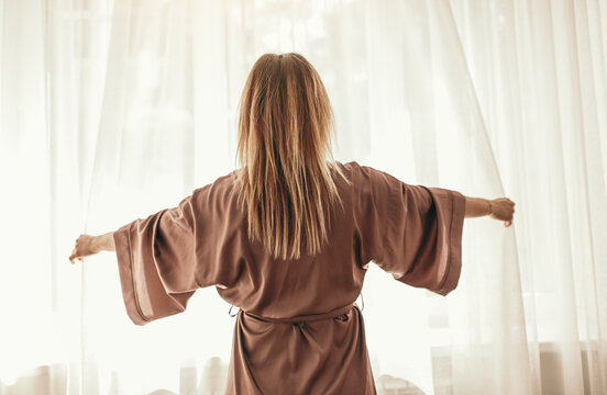 Woman waking up and opening curtains