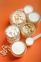 Nutrition supplements, glass of water and different vitamins such as vitamin C, magnesium, vitamin A, protein, electrolytes and collagen peptides in beautiful composition on orange bright background.