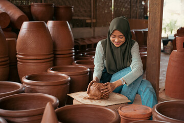 young woman in a hijab sits working clay into pottery