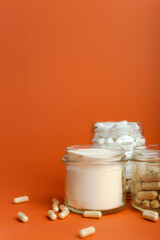 Various vitamin and mineral complexes in the form of capsules and in the form of powder in jars on an orange background. vitamin C, magnesium, vitamin A, protein, electrolytes and collagen peptides.