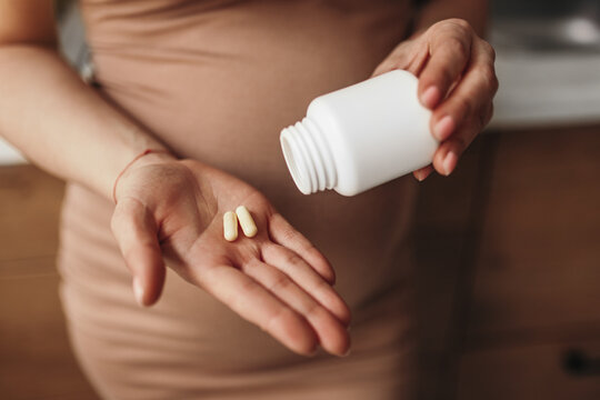 Crop pregnant lady drinking vitamin tablets