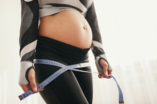 Anonymous pregnant woman making measurement with tape after workout