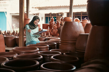veiled woman with pointing finger while using notepad counting pottery