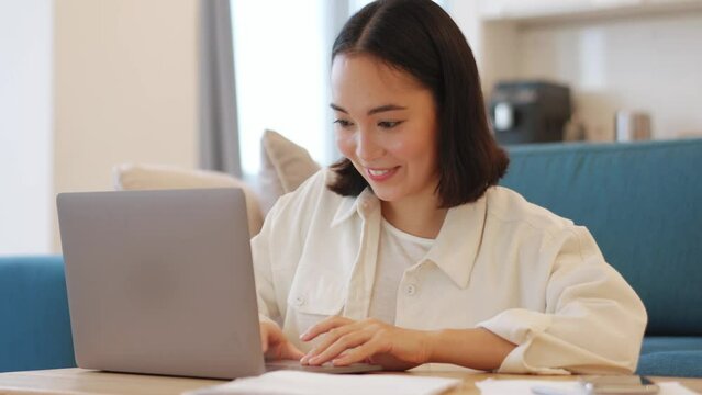 Cheerful Asian woman working on laptop at home