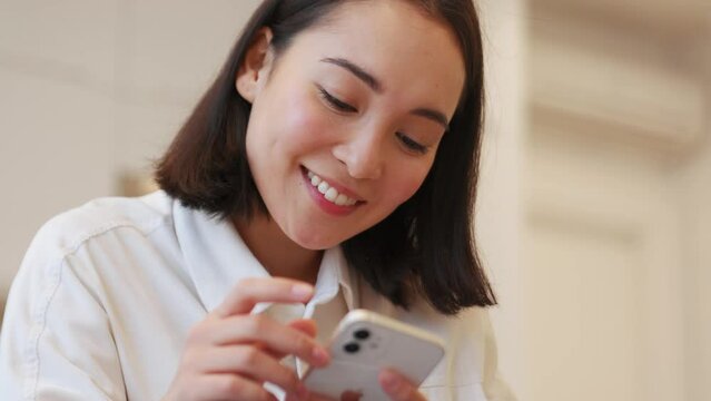 Smiling Asian woman texting by phone on the sofa