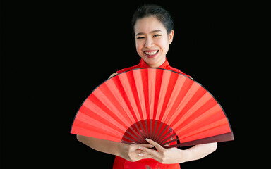 Young Chinese beautiful Asian woman wearing red traditional dress, holding folding fan, standing on black isolated background cutout, looking at camera, smiling to celebrate new year with copy space.