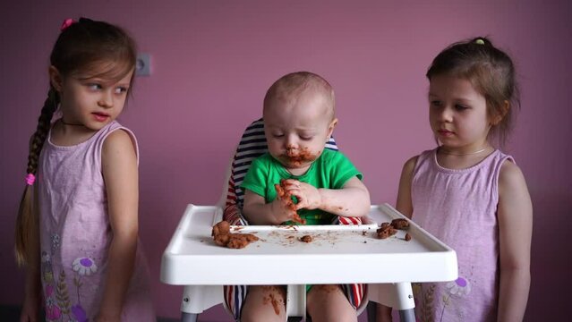 A small child eats chocolate. His face and hands are very dirty. Next to the baby are his sisters. The kid is happy. High quality FullHD footage