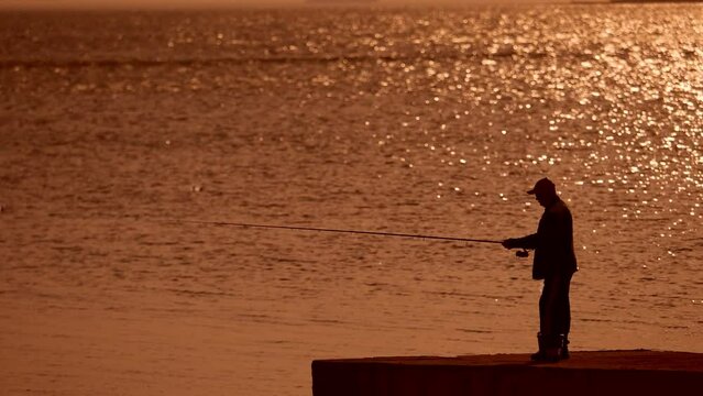 Silhouette of fisherman on sea bank against a sunset