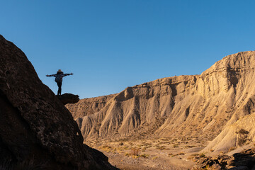 Silhouette of a free young woman with open arms climbing a rock in the desert of Tabernas, province of Almería, Andalusia. A trek in the Rambla Las Salinas