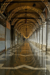 Die Weihnachtliche Beleuchtung spiegelt sich in den Arkaden am Markus Platz in Venedig in leichten Hochwasser der Nacht.