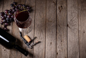 Wine background. Red wine in glass with grapes, corkscrew on a wooden background